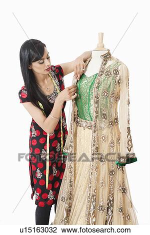 Stock Image - Indian female dressmaker working on a traditional outfit over gray background. Fotosearch