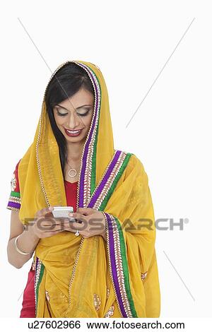 Stock Photograph - Indian female in traditional wear using cell phone over white background. Fotosearch