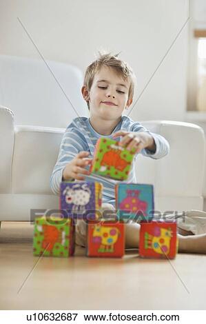 Stock Photo - Little boy stacking blocks while sitting on floor. Fotosearch