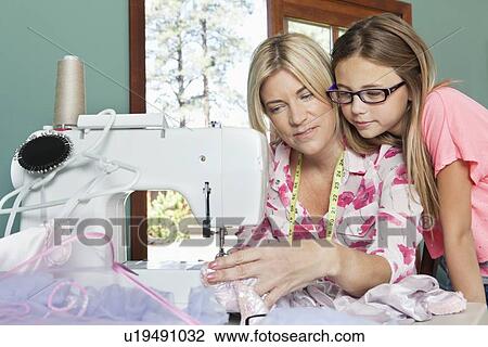 Stock Image - Little girl looking at mother sewing cloth. Fotosearch