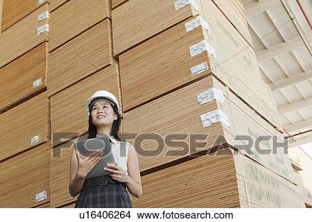 Low angle view of female industrial worker holding tablet PC with stacked wooden planks in background View Large Photo Image Picture - Low angle view of female industrial worker holding tablet PC with stacked wooden planks in background. Fotosearch