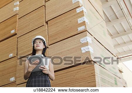 Low angle view of female industrial worker holding tablet PC with stacked wooden planks in background View Large Photo Image Picture - Low angle view of female industrial worker holding tablet PC with stacked wooden planks in background. Fotosearch