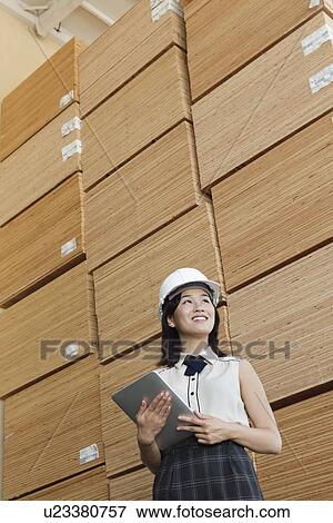 Low angle view of female industrial worker holding tablet PC with stacked wooden planks in background View Large Photo Image Stock Photo - Low angle view of female industrial worker holding tablet PC with stacked wooden planks in background. Fotosearch
