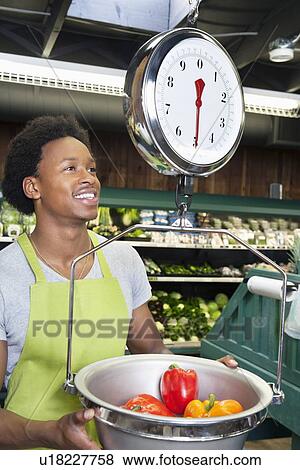 Stock Photo - Male African American store clerk weighing bell peppers on scale. Fotosearch