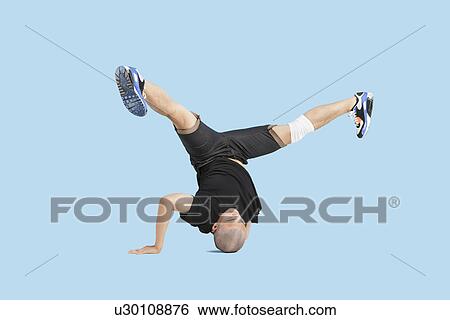 Stock Photograph - Male dancer doing head stand with legs spread apart over blue background. Fotosearch