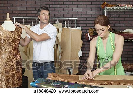 Stock Image - Male designer looking at coworker as she traces pattern on cloth in design studio. Fotosearch