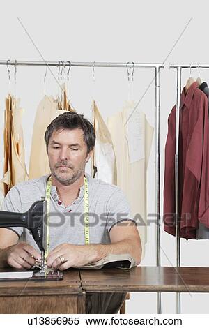 Male dressmaker stitching cloth on sewing machine with clothes rack in background View Large Photo Image Stock Photography - Male dressmaker stitching cloth on sewing machine with clothes rack in background. Fotosearch