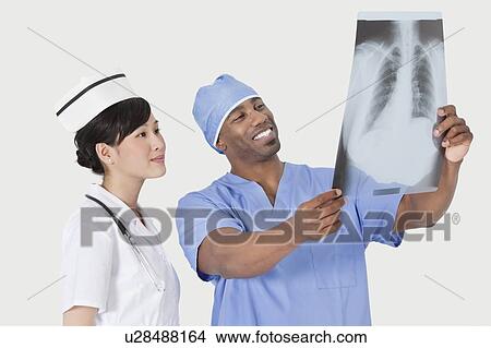 Male surgeon with nurse examining X-ray report over gray background View Large Photo Image Picture - Male surgeon with nurse examining X-ray report over gray background. Fotosearch