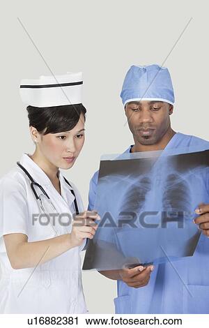 Male surgeon with nurse examining x-ray report over gray background View Large Photo Image Stock Image - Male surgeon with nurse examining x-ray report over gray background. Fotosearch