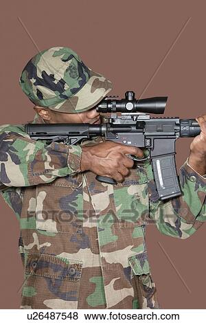 Stock Photo - Male US Marine Corps soldier aiming M4 assault rifle over brown background. Fotosearch