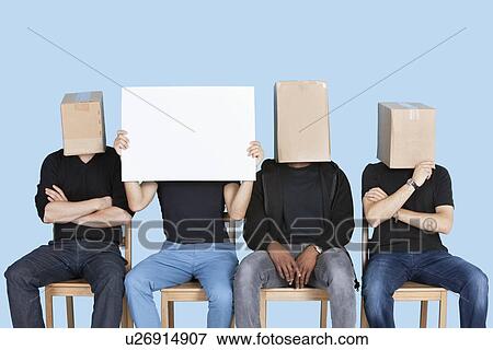 Stock Photo - Man holding blank cardboard with male friends faces covered with boxes over blue background. Fotosearch