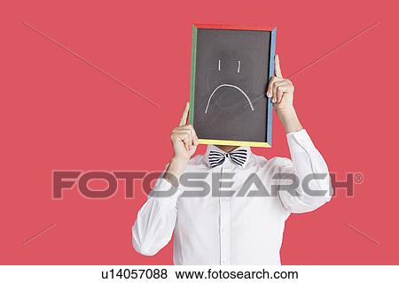 Man holding sad smiley face sign over red background View Large Photo Image Stock Photo - Man holding sad smiley face sign over red background. Fotosearch