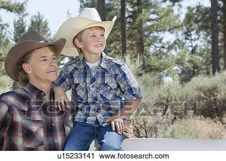 Mature father and son wearing cowboy hats looking away in park View Large Photo Image Stock Image - Mature father and son wearing cowboy hats looking away in park. Fotosearch