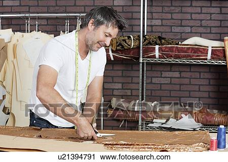 Stock Image - Mature male dressmaker cutting fabric in design studio. Fotosearch