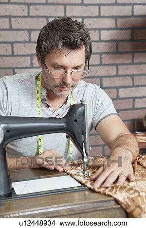 Picture - Mature male dressmaker stitching cloth on sewing machine. Fotosearch