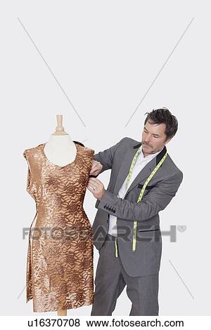Stock Photo - Mature male fashion designer adjusting cloth on tailor's dummy over gray background. Fotosearch
