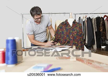 Stock Image - Mature male fashion designer taking measurement of shirt in design studio. Fotosearch