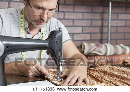 Stock Image - Mature male tailor stitching cloth on sewing machine. Fotosearch