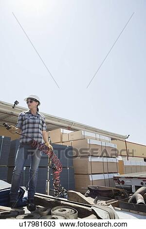 Stock Image - Mid adult woman holding a break hose while standing on logging truck. Fotosearch