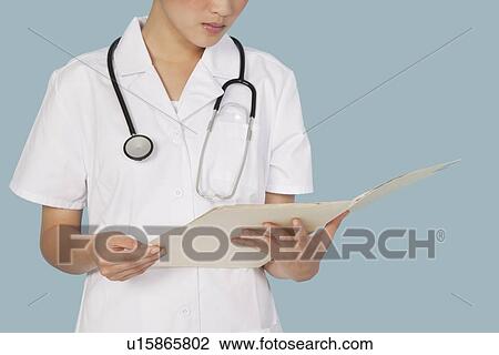 Stock Image - Midsection of a female doctor reading medical report over light blue background. Fotosearch