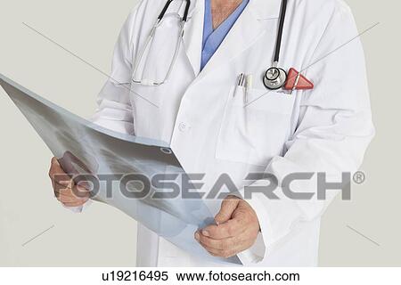 Stock Photography - Midsection of male doctor with x-ray report over gray background. Fotosearch