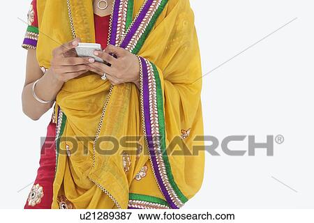 Stock Photo - Midsection of woman in Indian clothing using cell phone over white background. Fotosearch