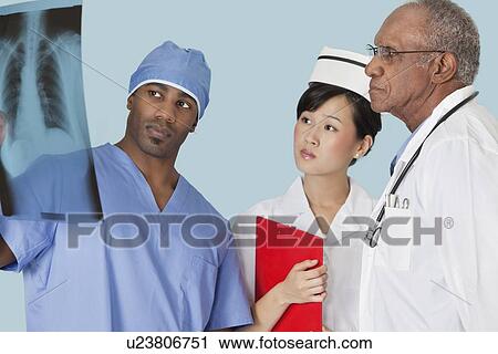 Multi ethnic doctors examining x-ray report over light blue background View Large Photo Image Stock Image - Multi ethnic doctors examining x-ray report over light blue background. Fotosearch