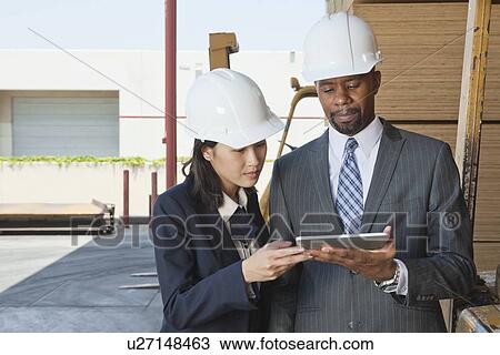 Stock Image - Multiethnic contractors using tablet PC at timber yard. Fotosearch