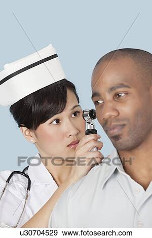 Nurse examining male patient's ear over light blue background View Large Photo Image Stock Photo - Nurse examining male patient's ear over light blue background. Fotosearch