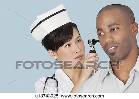 Stock Photography - Nurse examining male patient's ear over light blue background. Fotosearch
