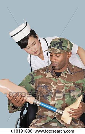Nurse with US Marine Corps soldier holding artificial limb as he sits in wheelchair over light blue background View Large Photo Image Stock Photograph - Nurse with US Marine Corps soldier holding artificial limb as he sits in wheelchair over light blue background. Fotosearch