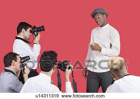 Stock Photo - Paparazzi taking photographs of male actor over red background. Fotosearch