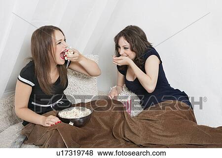 Stock Photo - Playful young women eating popcorn in bed. Fotosearch