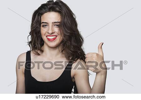 Portrait of a beautiful woman gesturing thumbs up over gray background View Large Photo Image Stock Image - Portrait of a beautiful woman gesturing thumbs up over gray background. Fotosearch