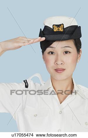 Picture - Portrait of a beautiful young US Navy officer saluting over light blue background. Fotosearch