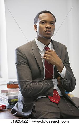 Portrait of a confident young businessman sitting on desk View Large Photo Image Picture - Portrait of a confident young businessman sitting on desk. Fotosearch