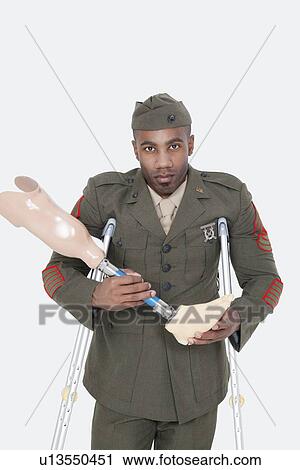 Stock Image - Portrait of a disabled US military officer holding prosthesis leg over gray background. Fotosearch