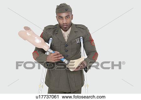 Stock Image - Portrait of a disabled US military officer holding prosthesis leg over gray background. Fotosearch