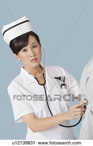 Stock Image - Portrait of a female doctor examining patient with stethoscope over light blue background. Fotosearch