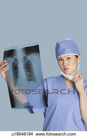 Portrait of a female surgeon holding x-ray report over light blue background View Large Photo Image Picture - Portrait of a female surgeon holding x-ray report over light blue background. Fotosearch