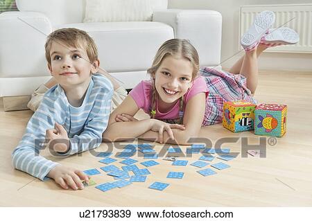 Stock Photo - Portrait of a girl and little brother lying on floor with cards. Fotosearch