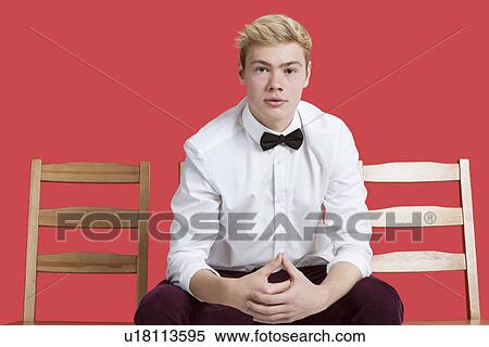 Portrait of a handsome young man in formal wear sitting on chair over red background View Large Photo Image Stock Photography - Portrait of a handsome young man in formal wear sitting on chair over red background. Fotosearch