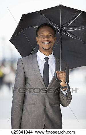 Portrait of a happy African American businessman holding umbrella View Large Photo Image Picture - Portrait of a happy African American businessman holding umbrella. Fotosearch