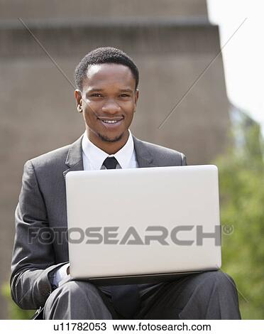 Stock Image - Portrait of a happy African American businessman using laptop. Fotosearch