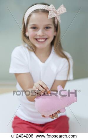 Portrait of a happy girl putting coin in piggy bank View Large Photo Image Stock Photograph - Portrait of a happy girl putting coin in piggy bank. Fotosearch