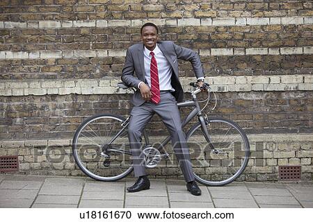 Portrait of a happy young businessman with bicycle against brick wall View Large Photo Image Stock Image - Portrait of a happy young businessman with bicycle against brick wall. Fotosearch