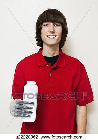 Stock Image - Portrait of a happy young man holding bottle with prosthetic hand over gray background. Fotosearch