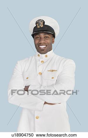 Stock Image - Portrait of a happy young US Navy officer standing with arms crossed over light blue background. Fotosearch