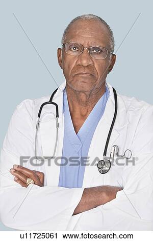 Portrait of a senior doctor with arms crossed over light blue background View Large Photo Image Stock Image - Portrait of a senior doctor with arms crossed over light blue background. Fotosearch