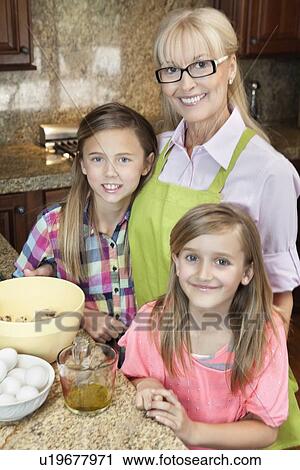 Stock Image - Portrait of a senior woman with granddaughters in kitchen. Fotosearch